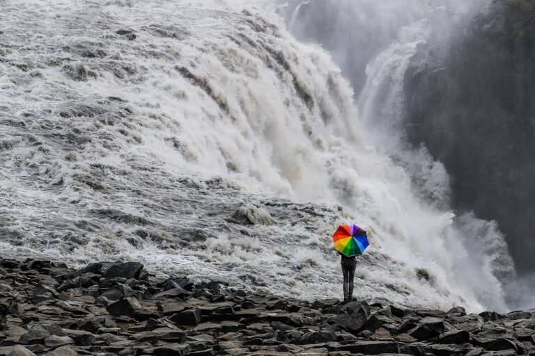 Człowiek z tęczowym parasolem u stóp wielkiego szarego wodospadu