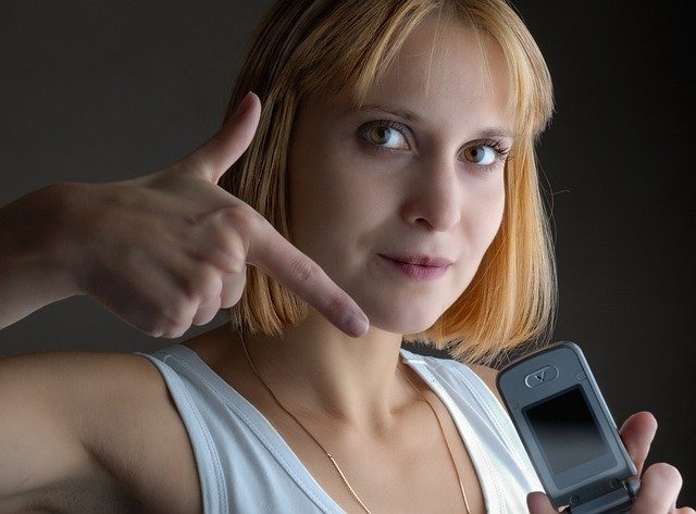 Twarz blondynki wskazującej palcem na ekran telefonu trzymanego w drugiej dłoni