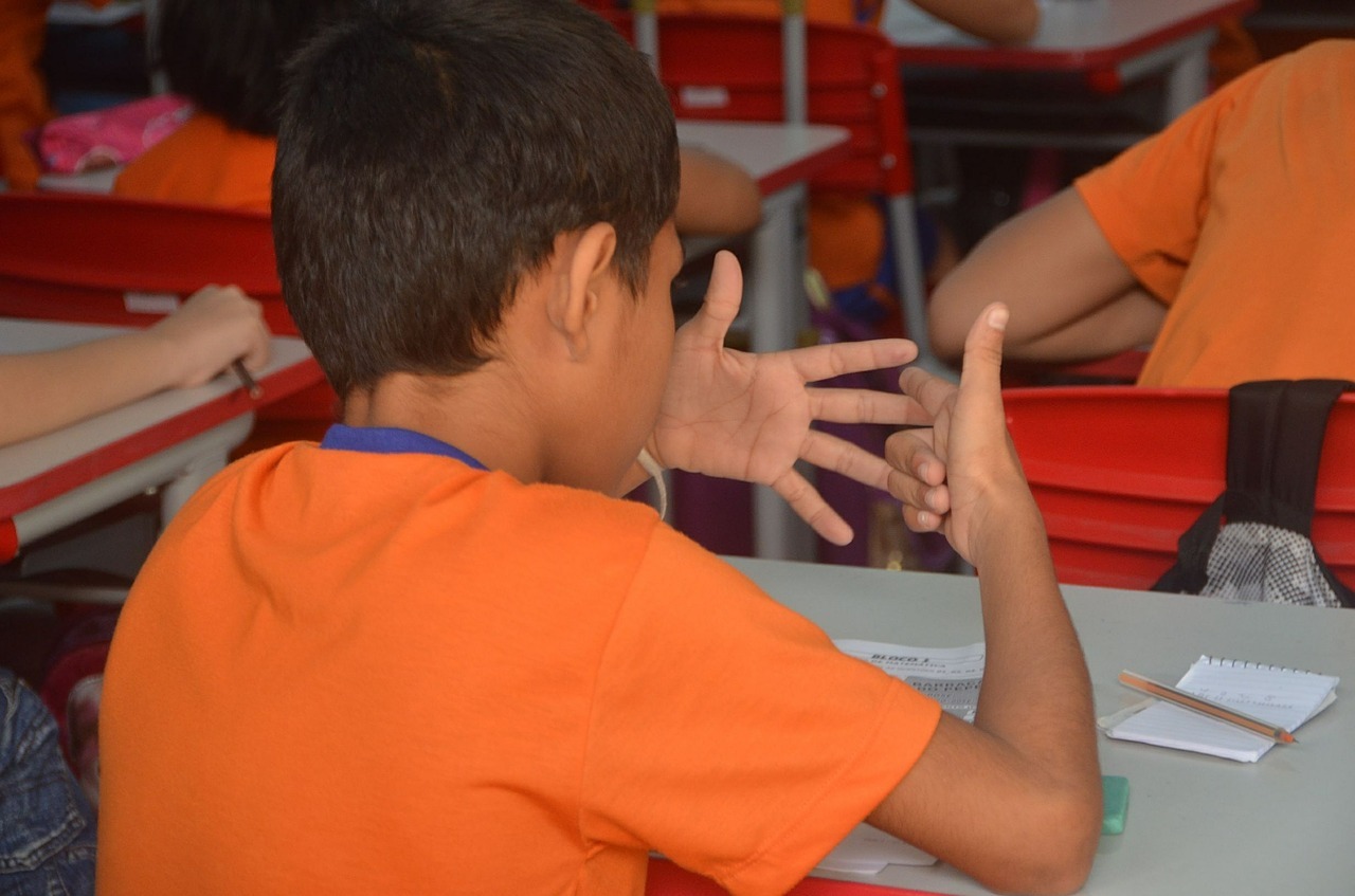 Chłopiec w pomarańczowej koszulce w ławce szkolnej liczy na palcach
